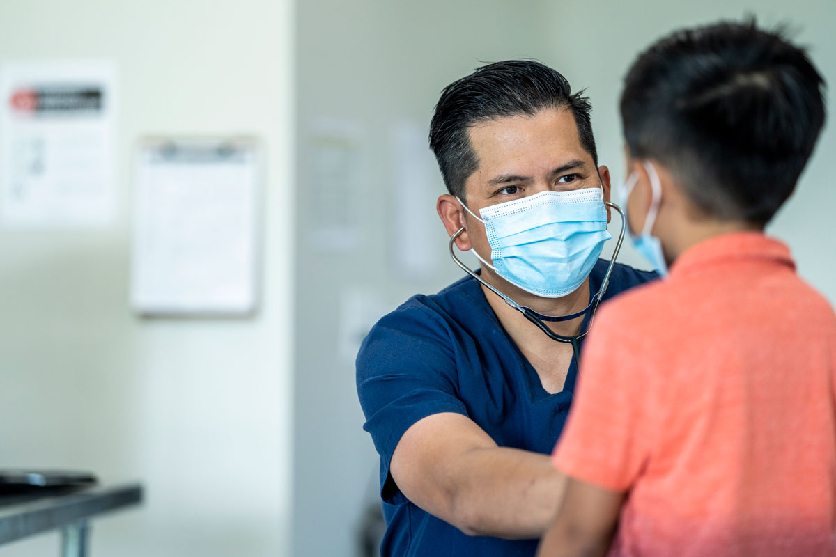 PDN medical nurse practicing healthcate in Mcallen while weearing a mask and gloves during a checkup with a young, 8 year old boy